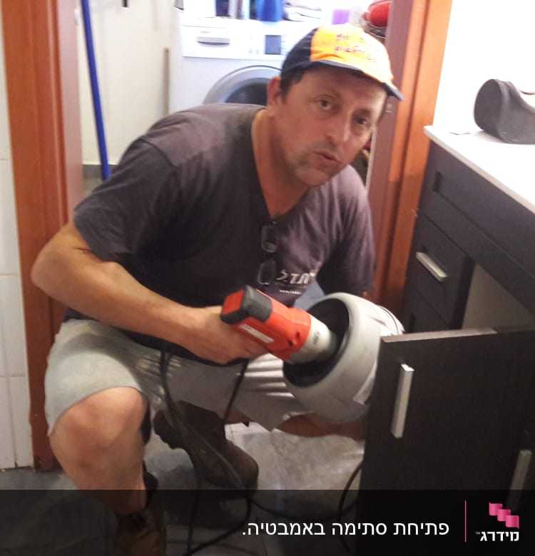 אדם מחזיק כלי עבודה ליד ארון פתוח בחדר אמבטיה